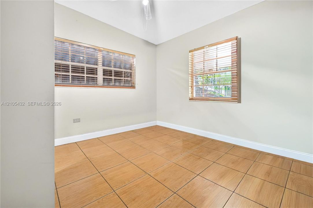 Neutral-toned interior featuring wood-finish tile flooring, vaulted ceilings, and dual windows equipped with horizontal blinds