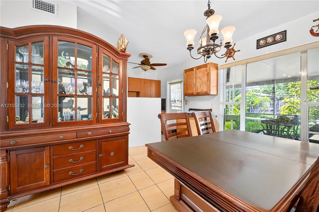 Dining area featuring ceramic tile flooring, a multi-arm chandelier, ceiling fan, and sliding glass doors with exterior screen enclosure