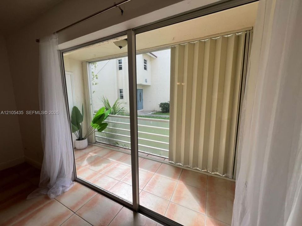 Sliding glass door opening to a tiled balcony with metal railing and accordion-style shutter