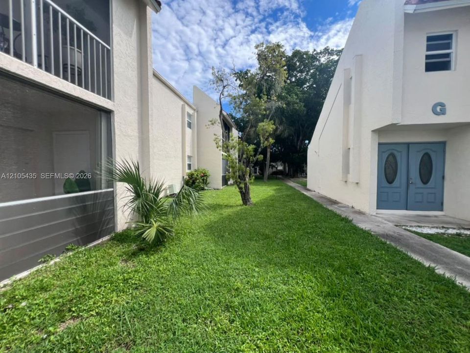 Stucco exterior featuring dual-entry doors, a screened-in balcony, concrete walkways, and mature landscaping