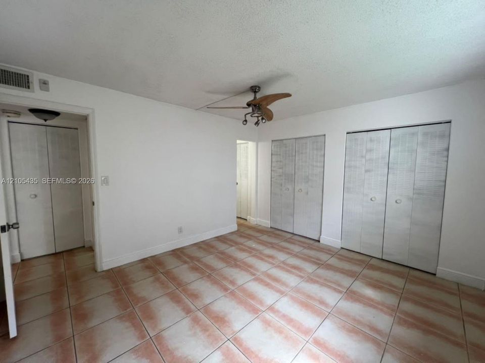 Room featuring neutral-toned tile flooring, three sets of bi-fold closet doors, and a multi-blade ceiling fan with integrated lighting