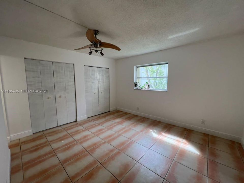 Room interior featuring ceramic tile flooring, dual closet sets with bi-fold doors, and a ceiling fan with integrated lighting