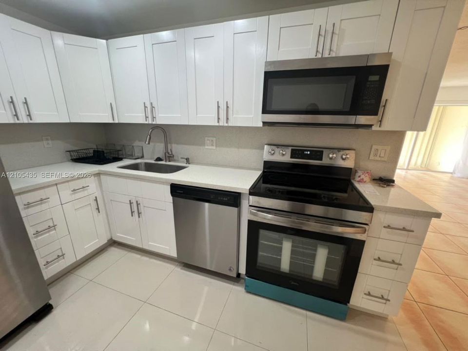 Kitchen featuring white shaker-style cabinetry, solid-surface countertops, stainless steel appliances, and tile flooring