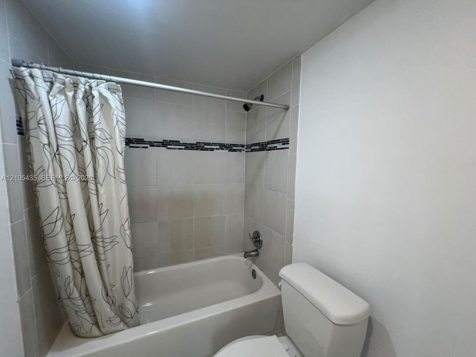 Full-size bathtub with tiled surround featuring a decorative mosaic inlay, integrated shower fixture, and standard toilet