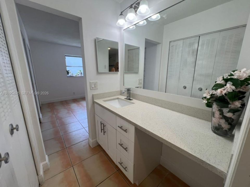 Bathroom vanity featuring white cabinetry, a light-toned solid surface countertop, an undermount rectangular sink, a single-handle chrome faucet, and a large wall-mounted vanity mirror