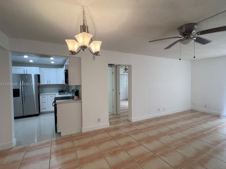 Open-concept interior featuring light-toned tile flooring, white cabinetry, a brushed metal three-light chandelier, and a ceiling fan with integrated lighting