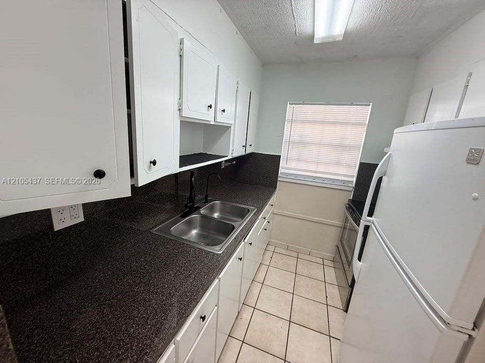 Kitchen featuring white cabinetry, dark speckled countertops, a double-basin stainless steel sink, and tile flooring