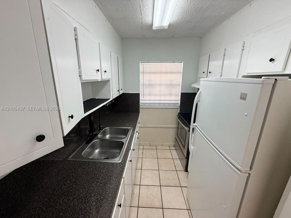 Galley kitchen featuring white cabinetry, dark speckled countertops, a double basin stainless steel sink, and tile flooring