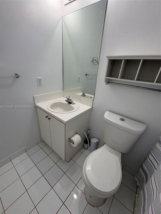 White tile flooring, wall-mounted rectangular mirror, vanity with integrated sink, and white toilet
