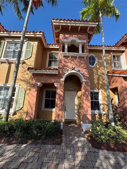 Mediterranean-style exterior featuring a clay tile roof, arched entryway, decorative stucco detailing, multi-pane windows with shutters, and a stone-paver walkway