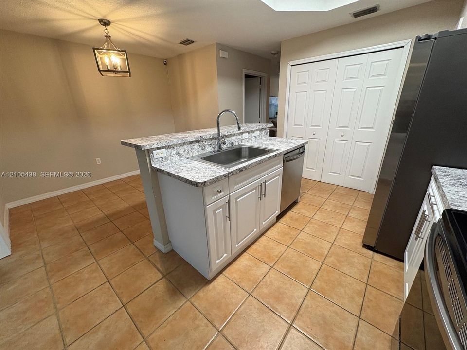 Kitchen featuring a central island with an undermount sink, a stainless steel dishwasher, and white cabinetry