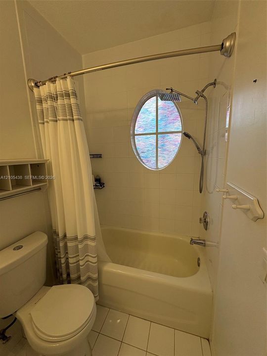 White tiled bathroom featuring an oval-shaped stained glass window, a built-in bathtub, and a dual-head shower system