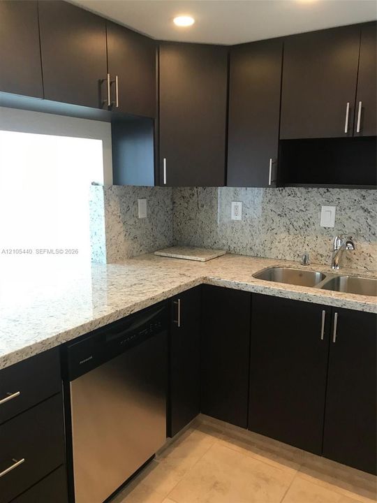 Modern kitchen featuring dark cabinetry, stainless steel dishwasher, double basin sink, and light-toned countertops with a matching backsplash