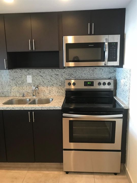 Granite countertops, stainless steel appliances, dark cabinetry with bar pulls, and a double basin sink