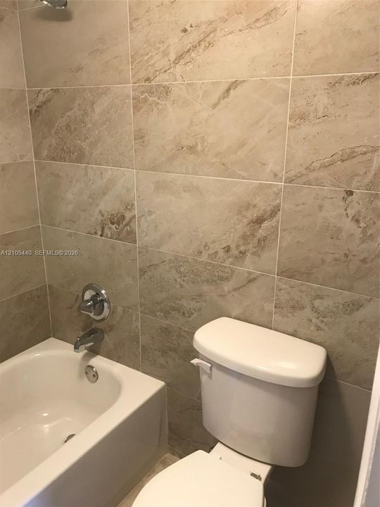 Bathroom featuring a built-in bathtub, chrome fixtures, and neutral-toned wall tiles
