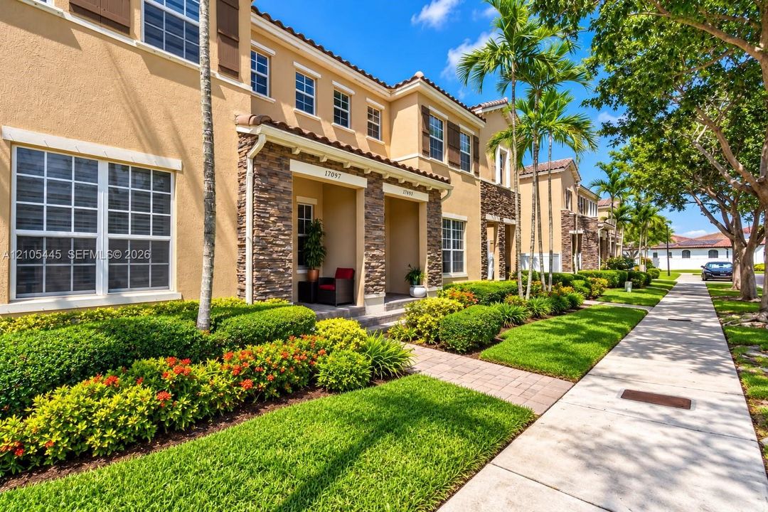 Multi-story exterior featuring a stucco facade, stone veneer accents, recessed entryway, and tiled roofline, complemented by landscaped grounds with palm trees