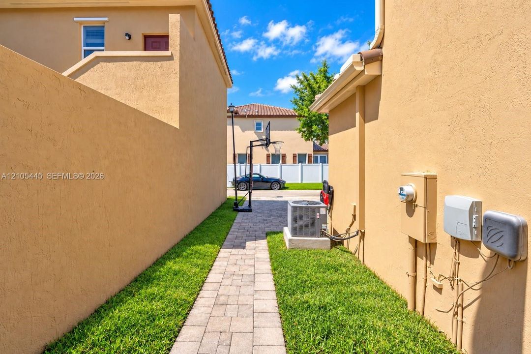 Exterior side corridor featuring stucco siding, paved walkway, and landscaped grass border
