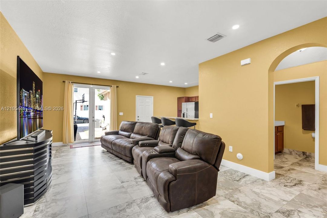 Neutral-toned interior featuring large-format stone-patterned tile flooring, recessed ceiling lighting, arched entryway, and double glass-paneled exterior doors