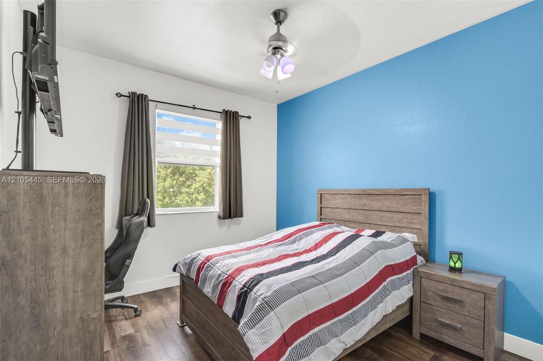 Wood-finish flooring, accent wall, ceiling fan with light fixture, and window with dual-track hardware