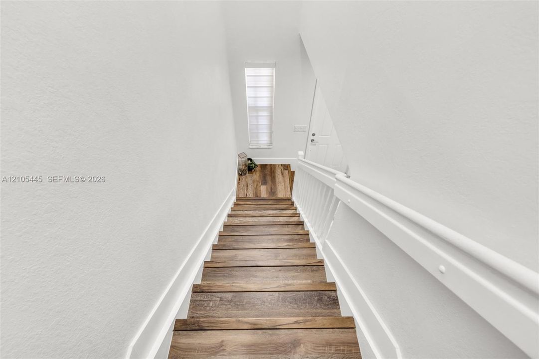 Staircase featuring wood-finish treads, crisp white wall paneling, and a white handrail