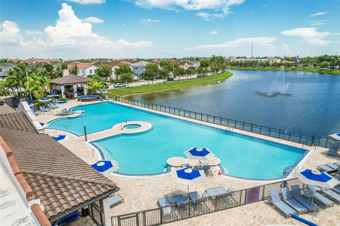 Swimming pool with a central spa, expansive paver deck, and covered pavilion, overlooking a lake with a fountain