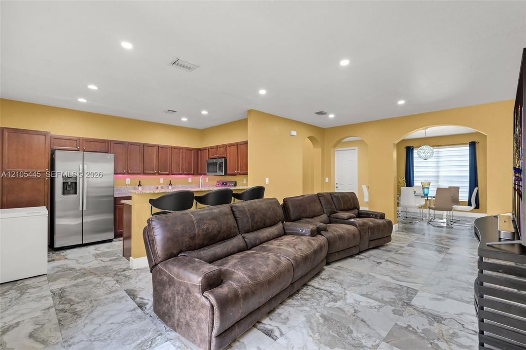Kitchen area featuring stained wood cabinetry, stone countertops, stainless steel appliances, recessed ceiling lighting, and large-format tile flooring