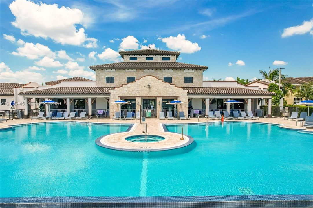 Community pool facility featuring a stone-clad building with a tile roof, an integrated circular spa, and a paved deck