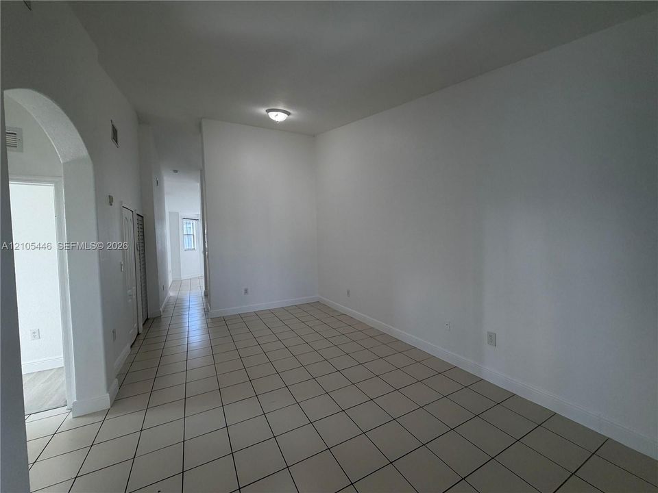 Spacious room featuring tile flooring, neutral wall tones, arched entryway, and flush-mount ceiling lighting