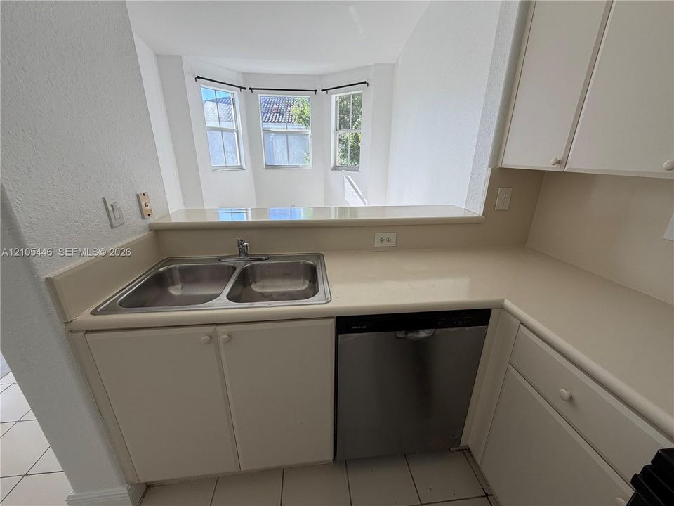 Double stainless steel sink, solid surface countertops, built-in dishwasher, white cabinetry, and bay windows