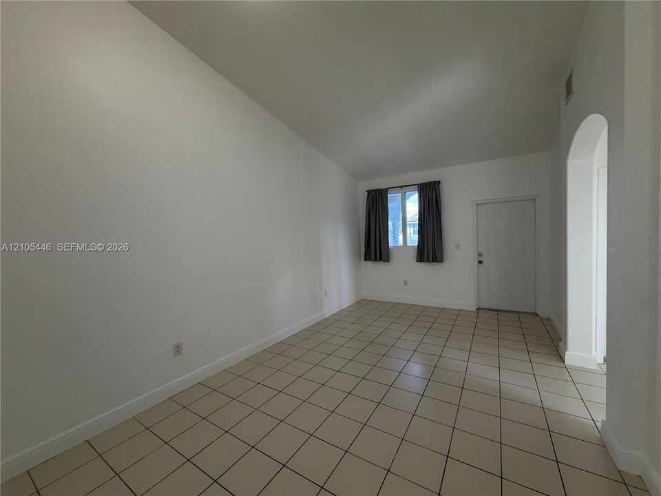 Tiled flooring throughout with a window featuring dark curtains, and a white door