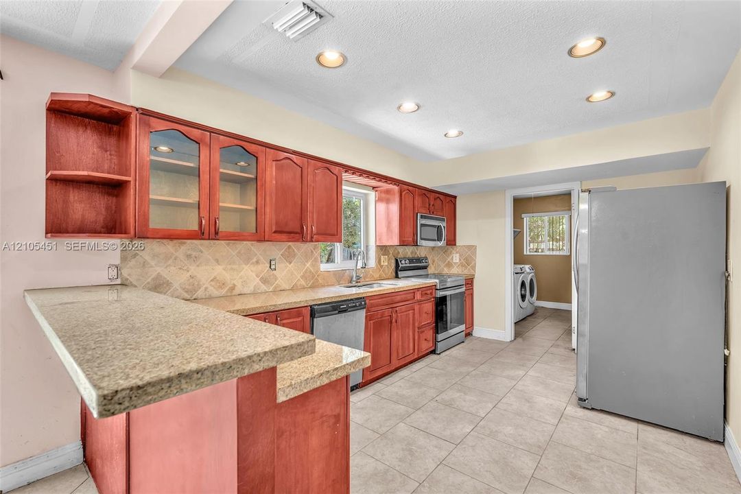 Kitchen featuring wood cabinetry, stone-surface countertops, tile backsplash, tile flooring, and recessed lighting