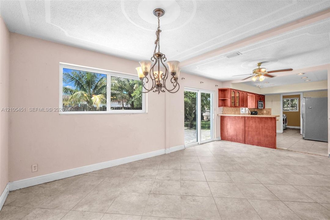 Dining area featuring large-format ceramic tile flooring, a decorative ceiling medallion with a multi-light chandelier, sliding glass doors, and a breakfast bar