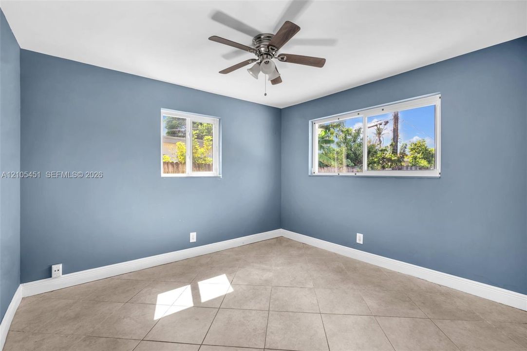 Room featuring tile flooring, neutral wall paint, two sliding windows, and a multi-blade ceiling fan with integrated lighting