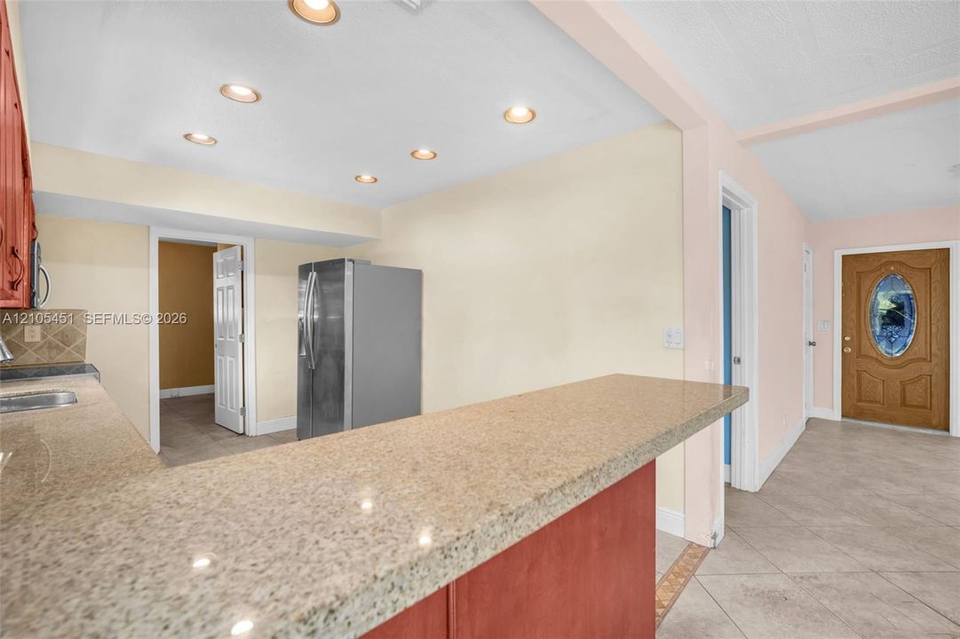 Kitchen featuring a stone-look countertop breakfast bar, recessed lighting, tile flooring, and a solid wood front door with an oval glass insert