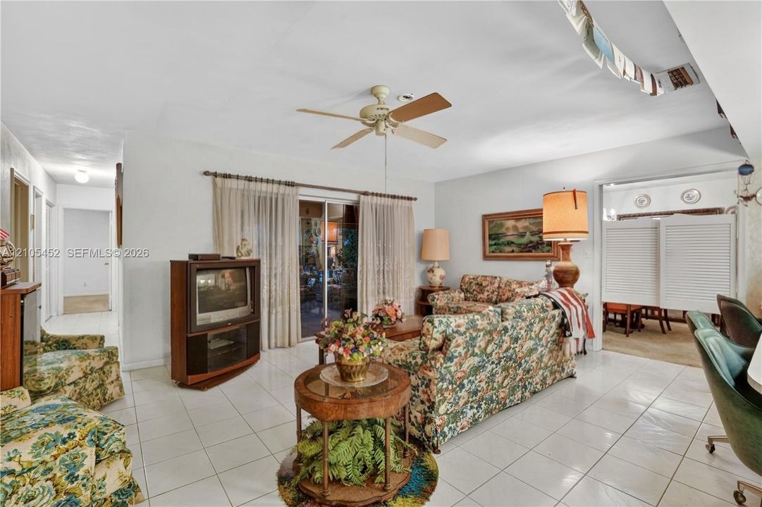 Living area featuring ceramic tile flooring, a ceiling fan with integrated lighting, and glass sliding doors