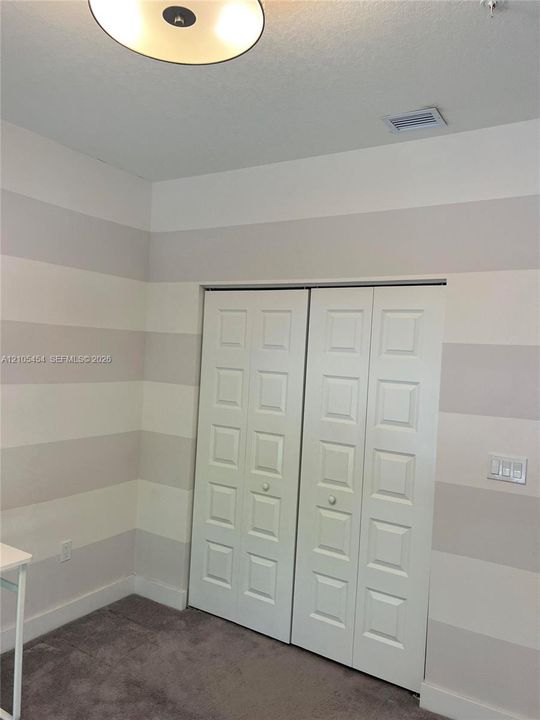 Recessed panel bifold closet doors, striped wall treatment, ceiling light fixture, and plush carpeting