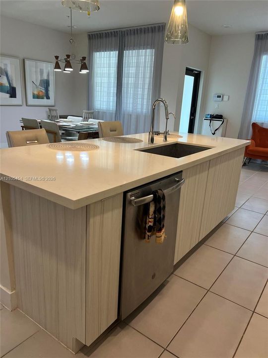 Kitchen island featuring a single-basin sink, gooseneck faucet, integrated dishwasher, and light-toned cabinetry
