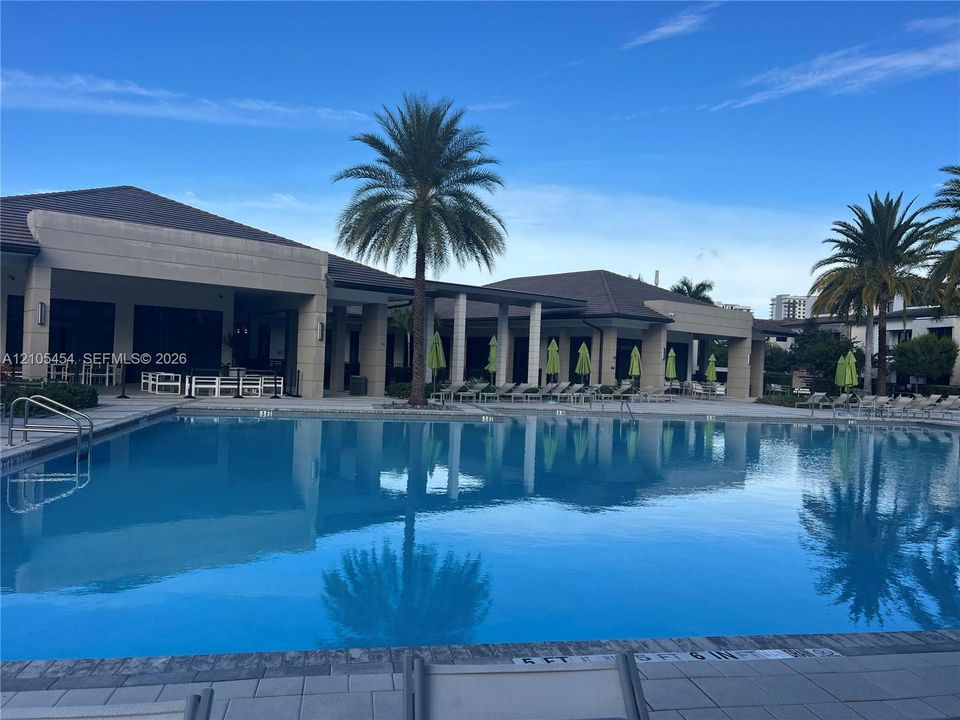 Expansive outdoor pool with integrated steps, surrounded by a paved deck and a covered patio area with recessed lighting