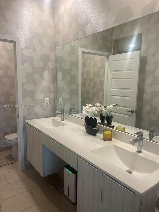 Dual rectangular basin vanity with chrome faucets, a full-width mirror, and geometric pattern wall covering