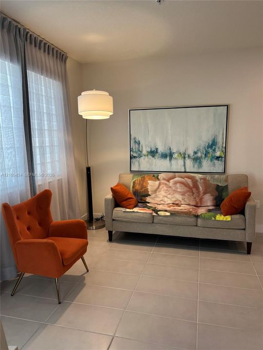 Light-colored wall finishes, full-height window with sheer drapes, recessed ceiling light, tile flooring, and a contemporary floor lamp