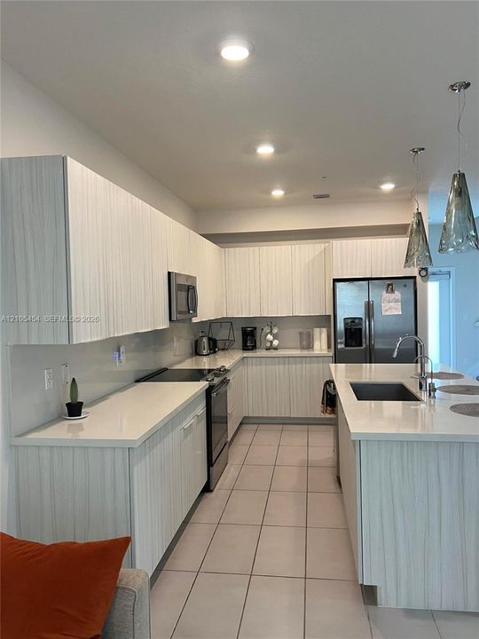 Contemporary kitchen featuring white cabinetry, light-toned countertops, stainless steel appliances, and an island with an integrated sink