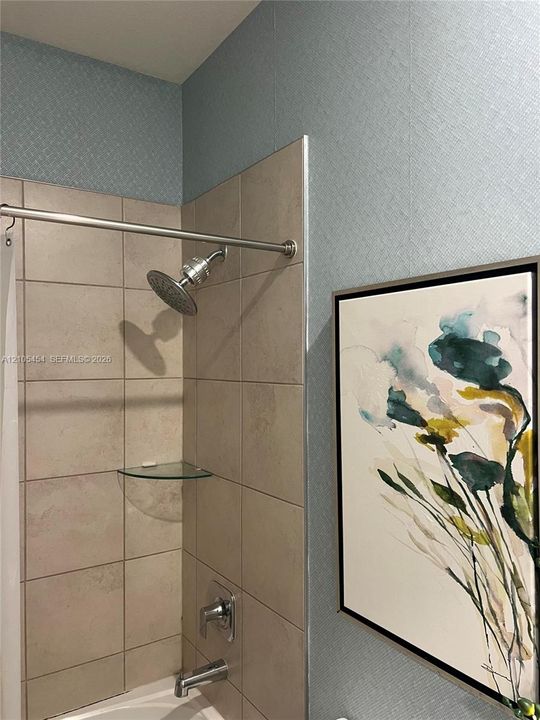 Bathtub with a tiled surround, a glass corner shelf, a brushed nickel showerhead, and a matching tub spout