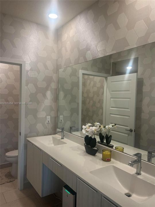 Dual vanity with integrated sinks, modern wall-mounted cabinetry, expansive mirror, and recessed lighting