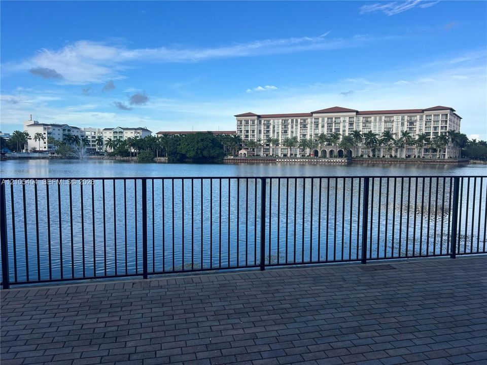 Paved waterfront promenade with metal railing overlooking the water and distant multi-story buildings