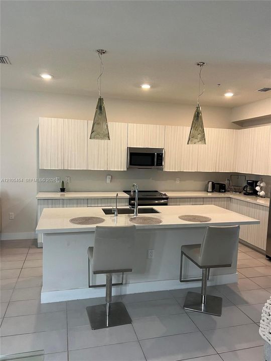 Modern kitchen featuring white cabinetry, a large kitchen island with integrated sink, recessed lighting, and two pendant light fixtures
