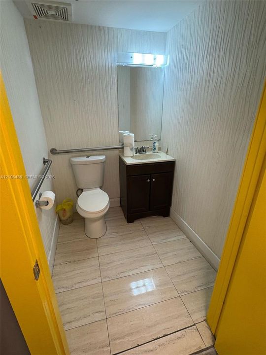 Bathroom featuring large-format tile flooring, a dark wood-finish vanity with a stone countertop, an integrated sink, and wall-mounted metal support bars
