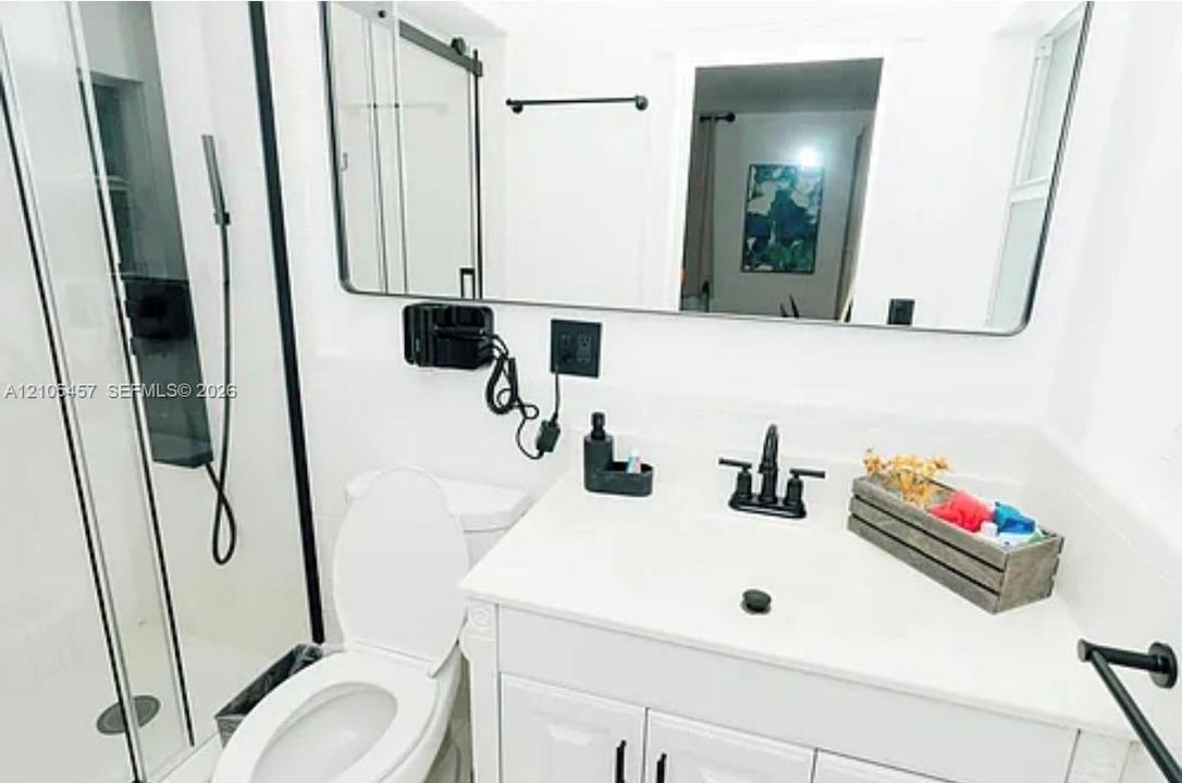 Bathroom featuring a white vanity cabinet with a solid surface countertop, matte black widespread faucet, rectangular mirror with a black frame, and a walk-in shower with a matte black trim and hardware