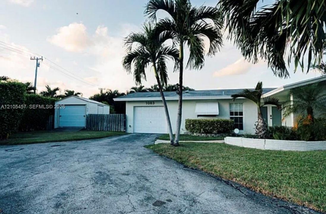 Single-story exterior featuring a painted stucco facade, attached garage, detached storage structure, and low-profile concrete block retaining wall