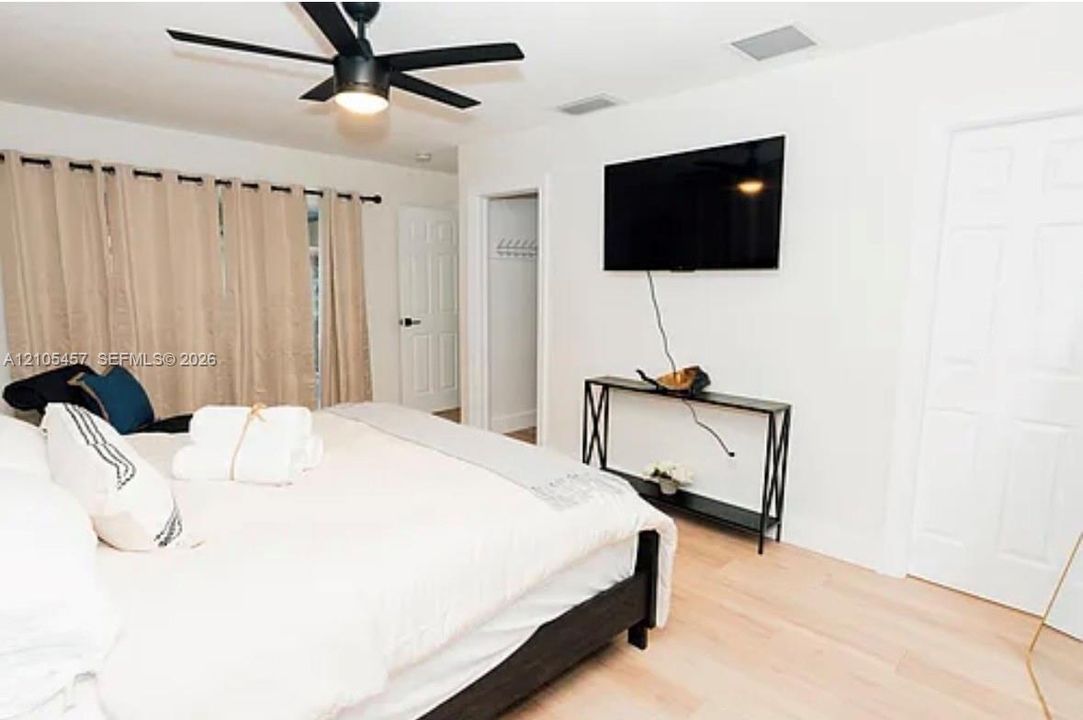 Bedroom featuring light-tone wood-finish flooring, matte black ceiling fan with integrated lighting, and white six-panel interior doors