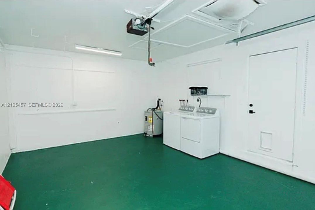 Garage space featuring painted concrete flooring, white walls, overhead lighting, an automated door opener system, and a dedicated laundry area
